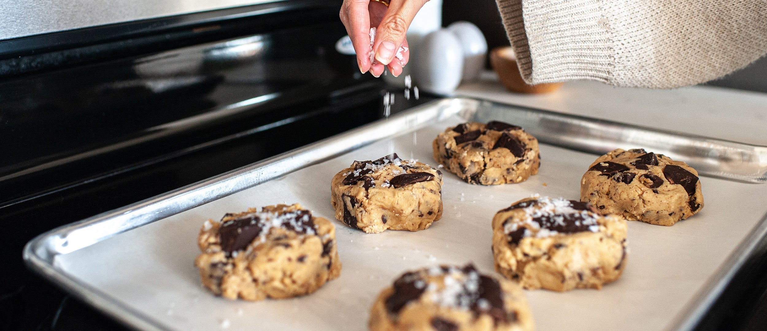 cookie dough on a baking sheet with hand sprinkling flaky salt