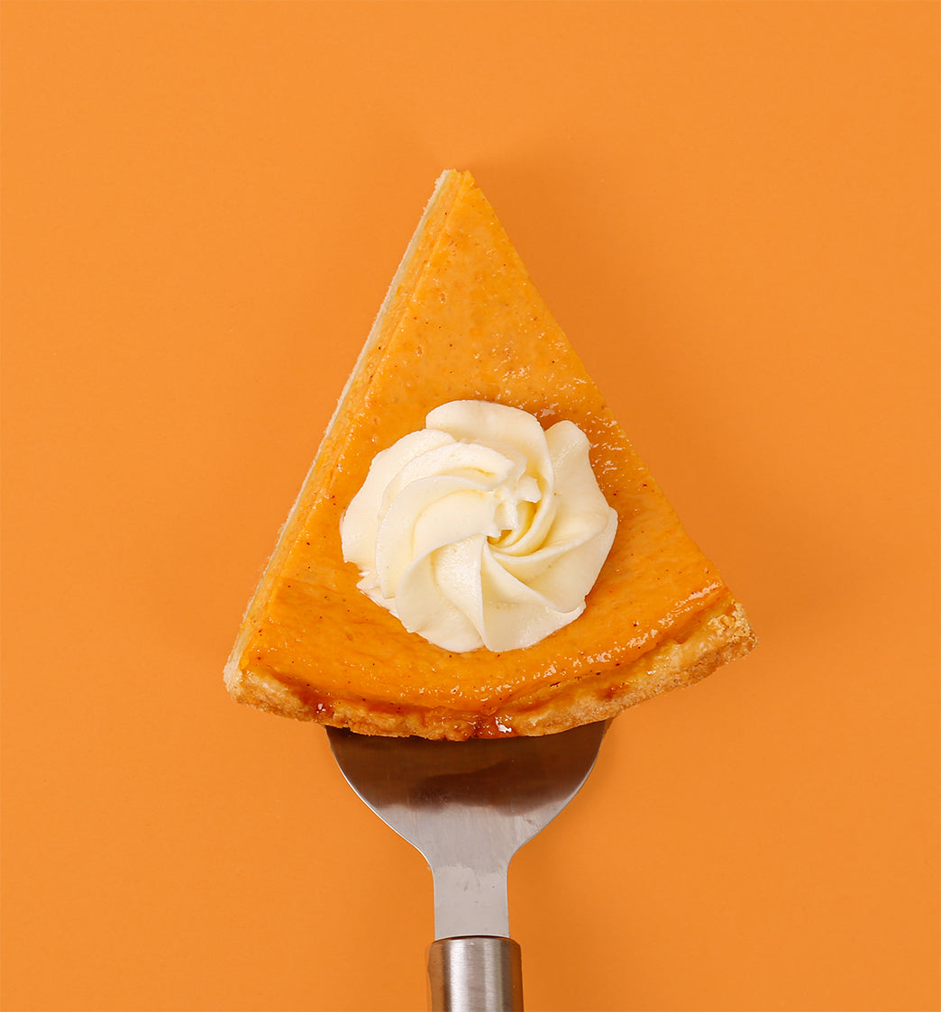 Slice of pumpkin pie with whipped cream on a fork against an orange background