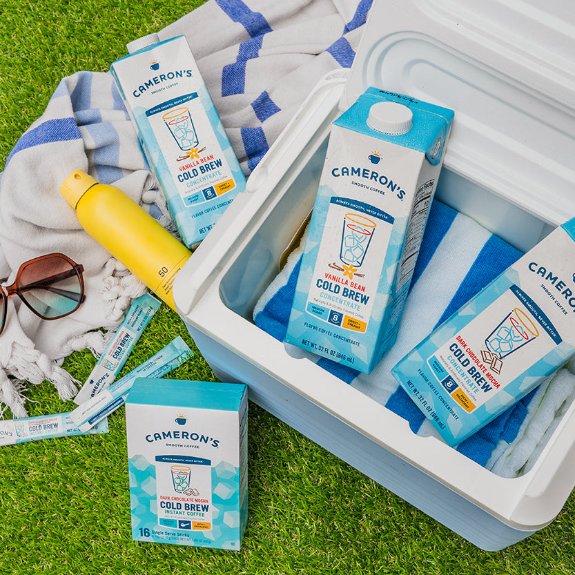Cameron's Cold Brew coffee boxes in a cooler with a yellow water bottle and sunglasses on grass.