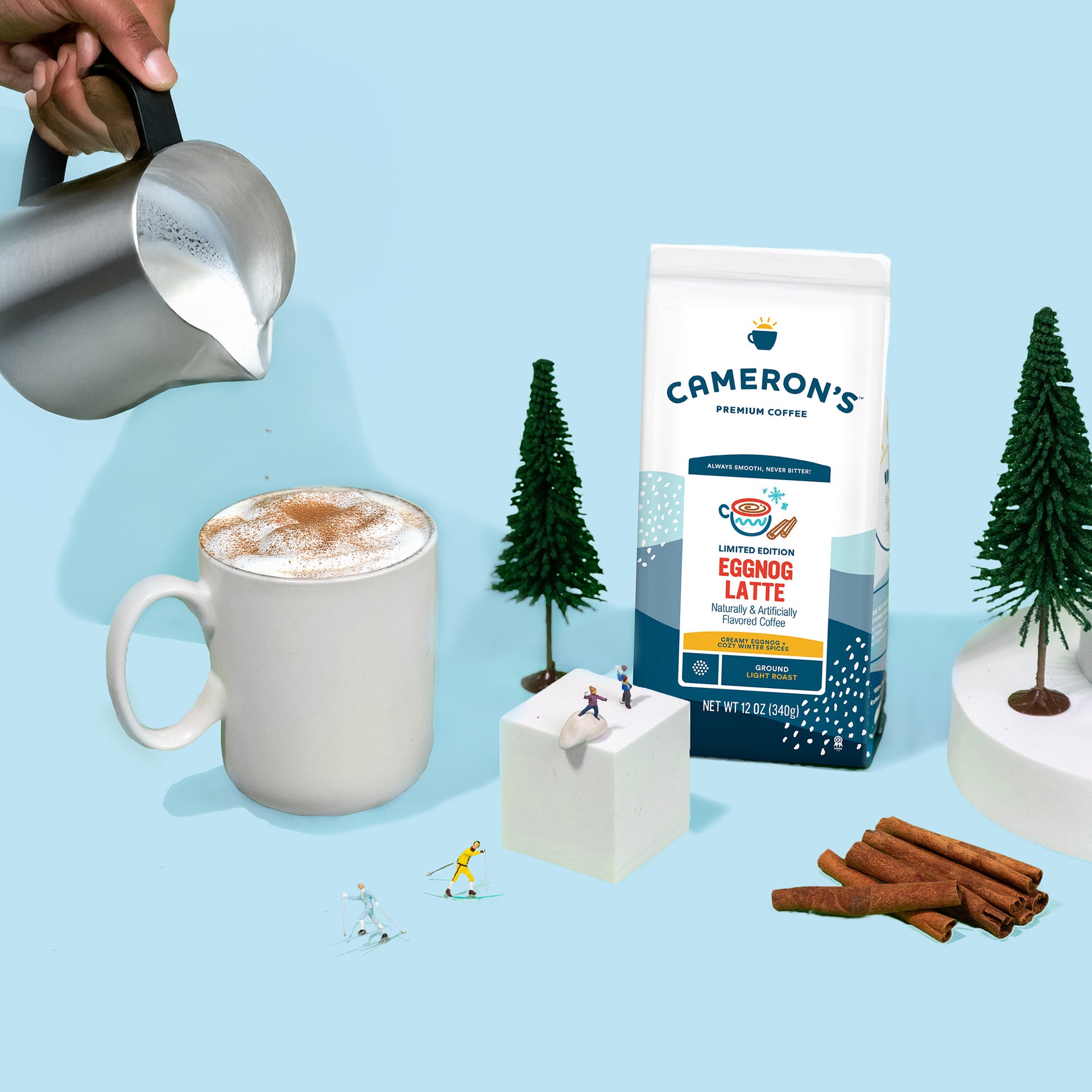 Cameron's Eggnog Latte coffee package with a mug of latte, cinnamon sticks, and decorative trees on a light blue background.