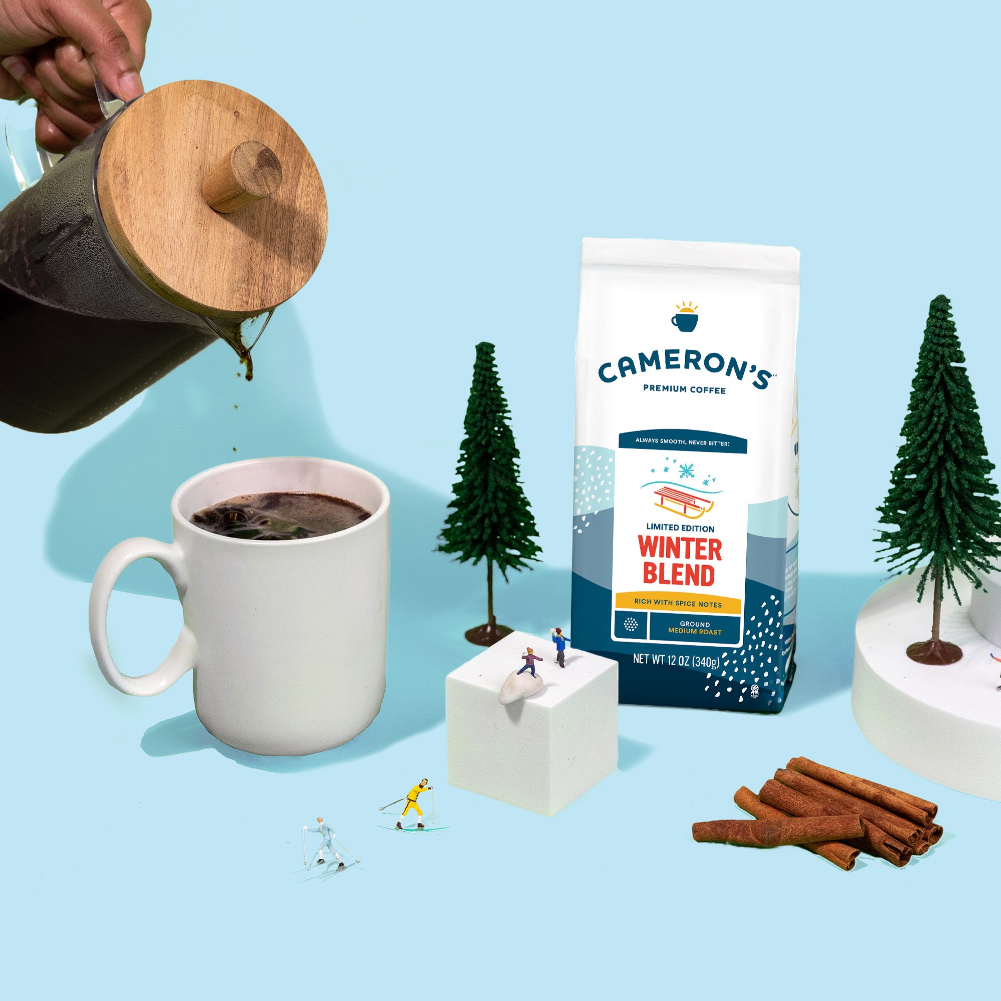 Cameron's Coffee Winter Blend package with a mug of coffee, cinnamon sticks, and decorative trees on a blue background