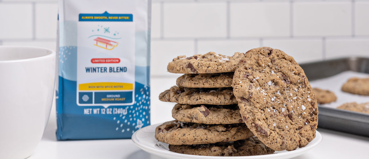 Chocolate chip cookies stacked in front of a Cameron's Coffee winter blend bag