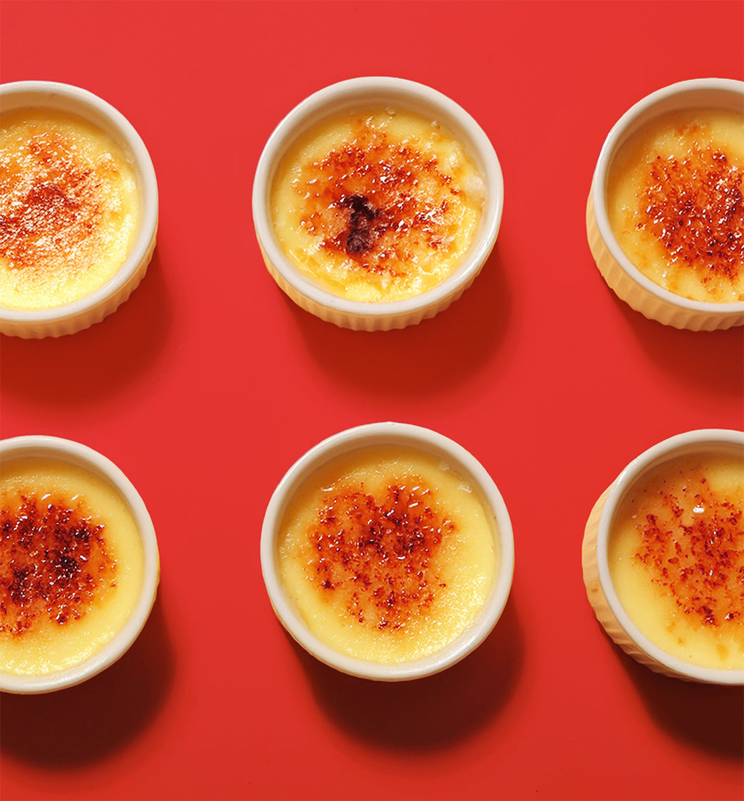 Multiple ramekins of creme brèleé with a caramelized top on a red background