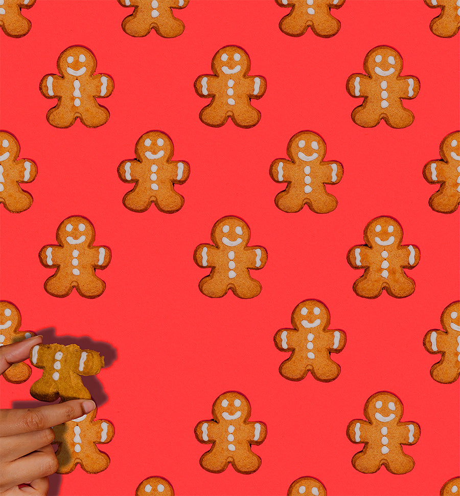 Pattern of gingerbread men cookies on a red background with a hand holding a cookie.