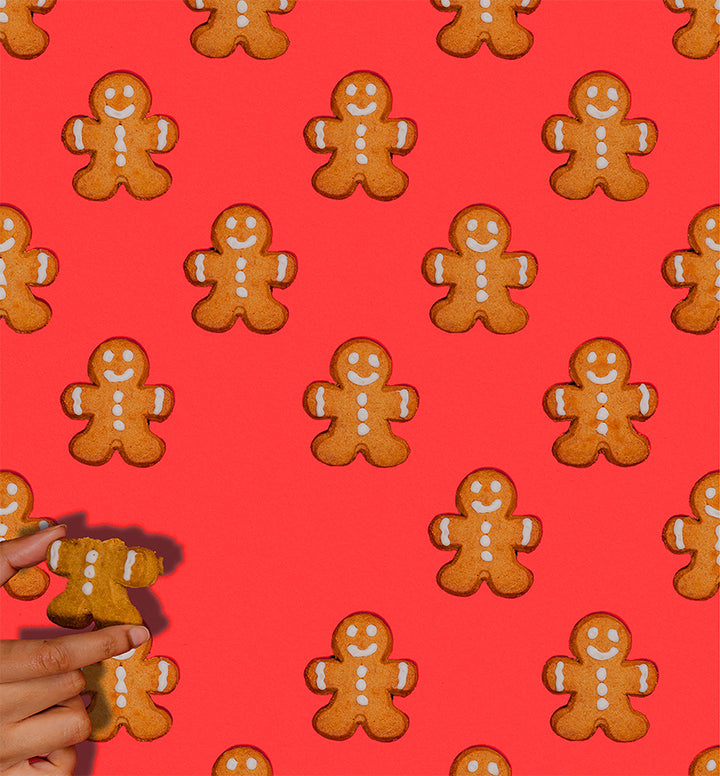 Pattern of gingerbread men cookies on a red background with a hand holding a cookie.