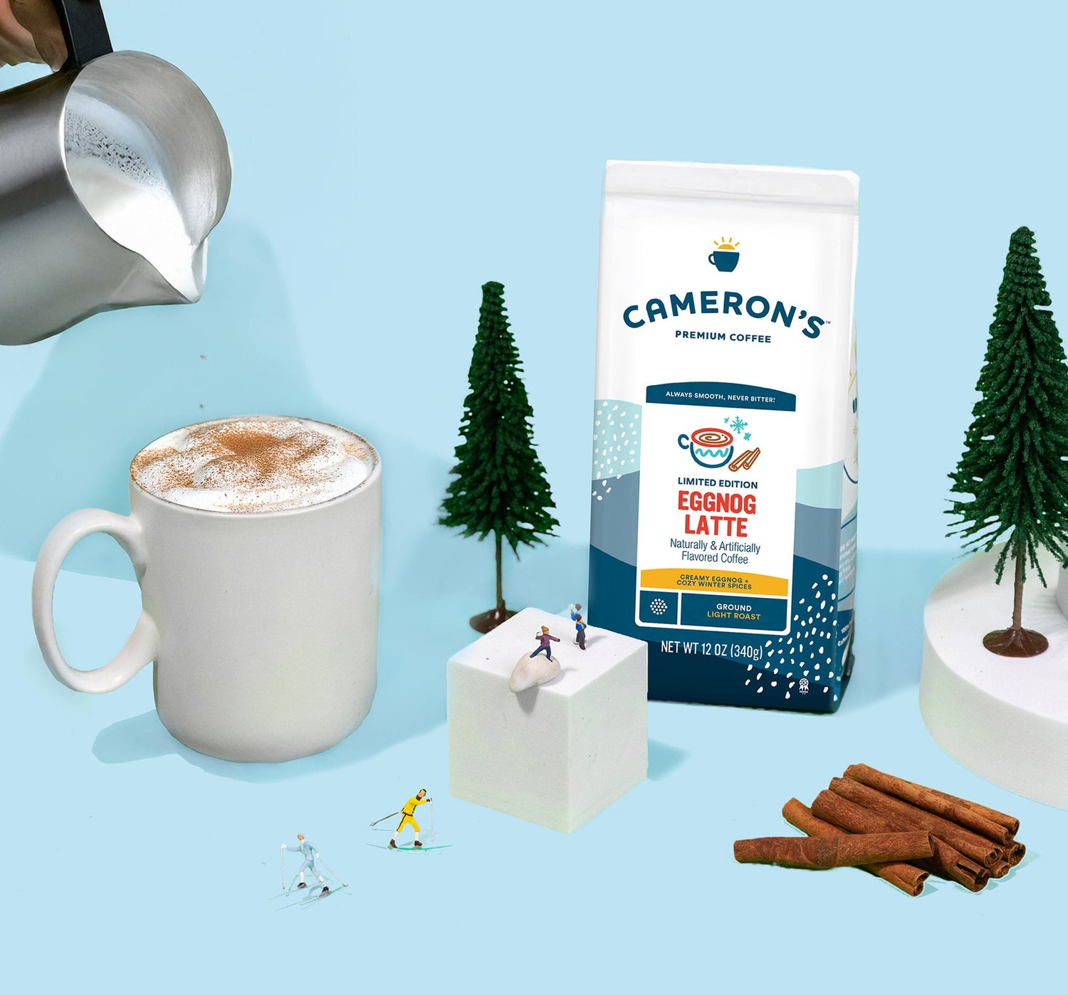 Cameron's Eggnog Latte coffee package with a mug, cinnamon sticks, and decorative trees on a light blue background.