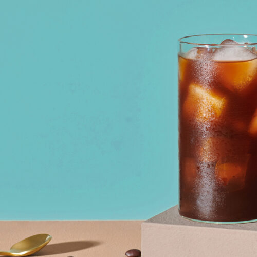 tall glass of cold brew with ice cubes on a blue background