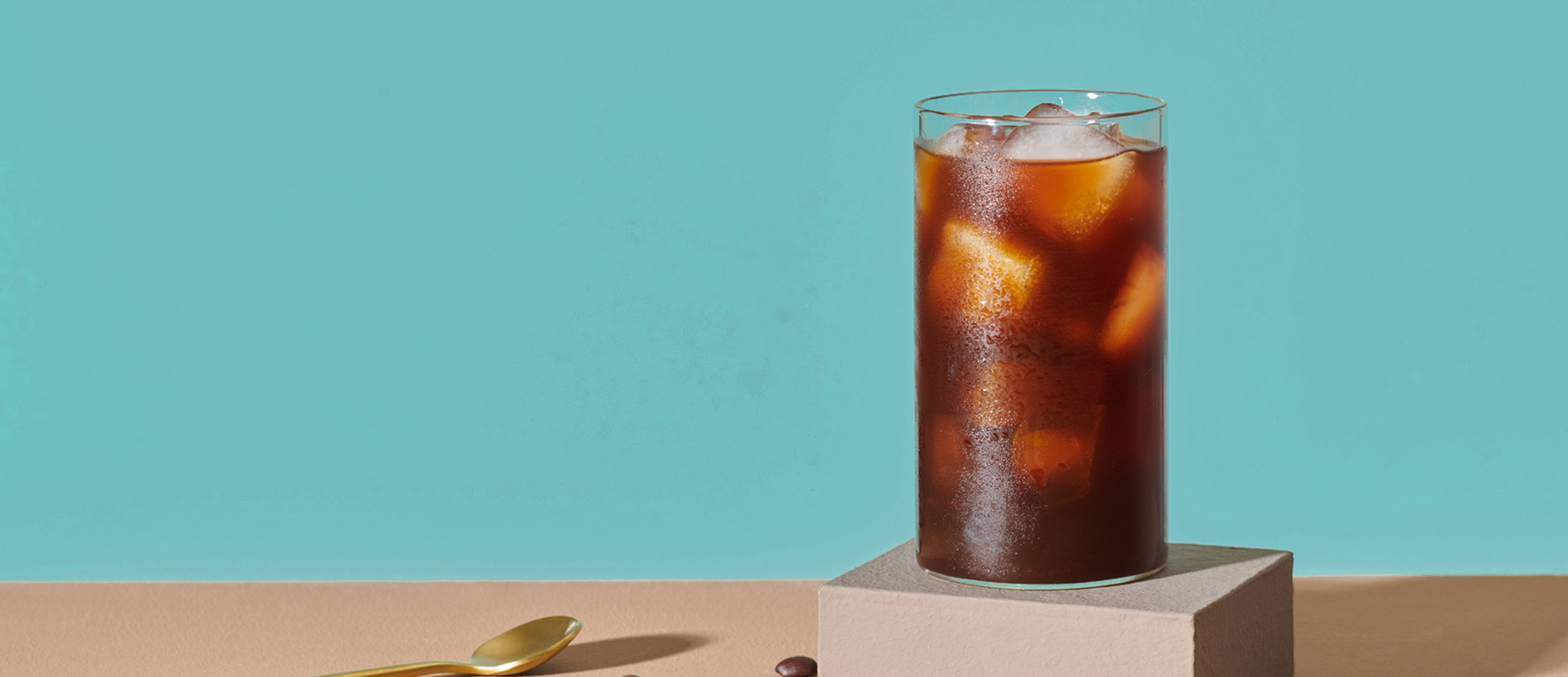 tall glass of cold brew with ice cubes on a blue background