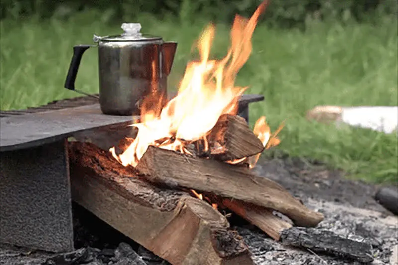 Coffee percolator sitting next to a campfire